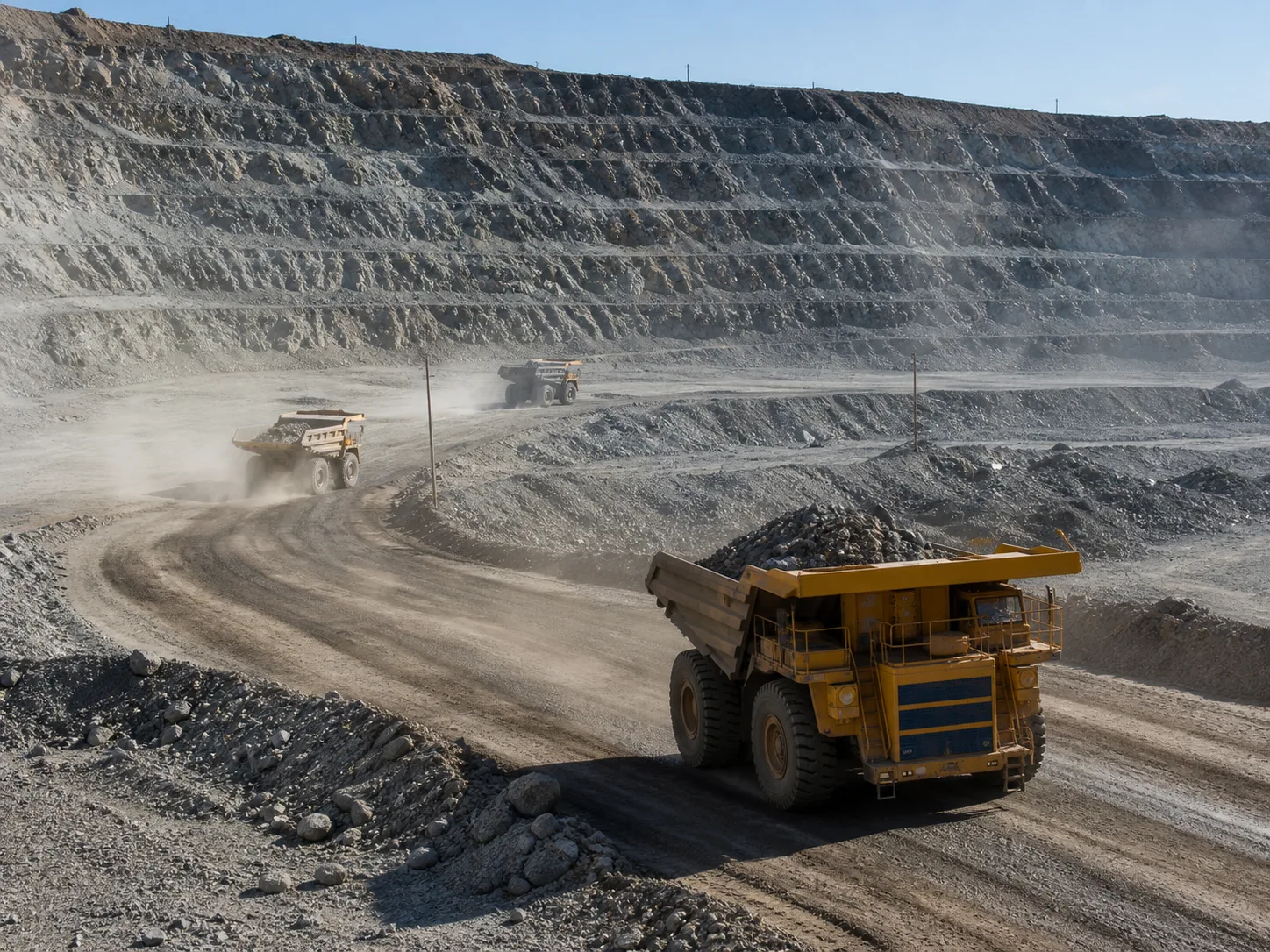 Open-pit mining operation with haul trucks moving through dusty terraces.